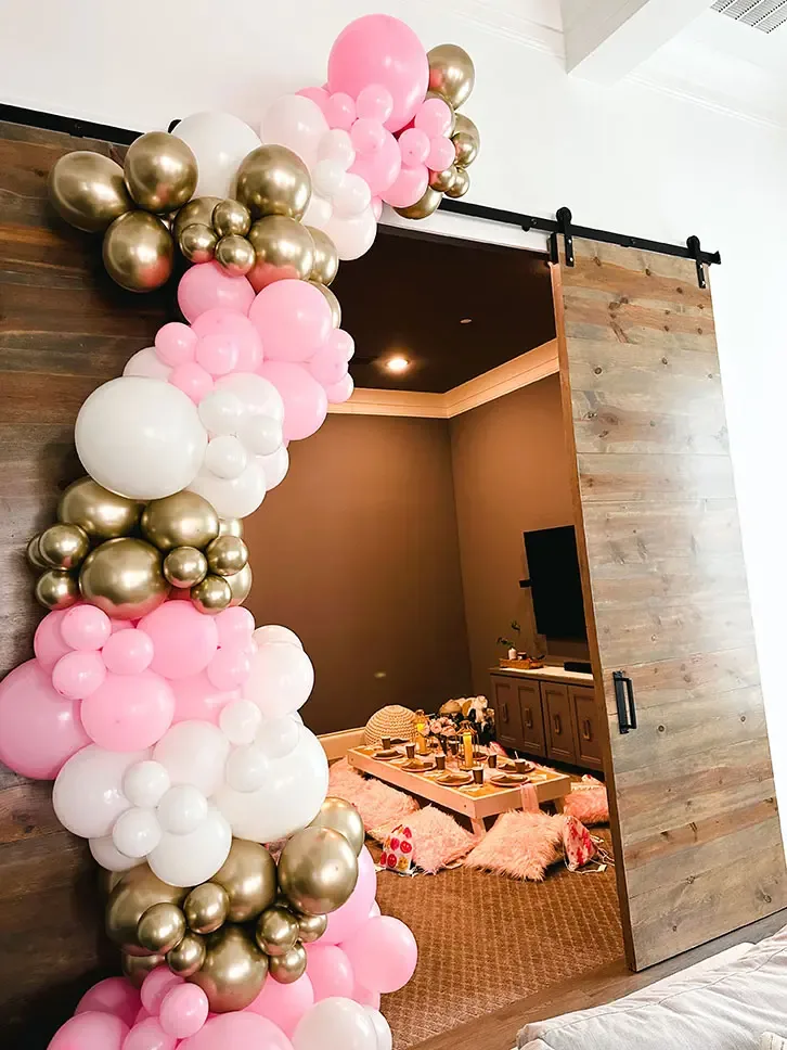 Pink, white and gold balloon garland framing a doorway into a picnic room