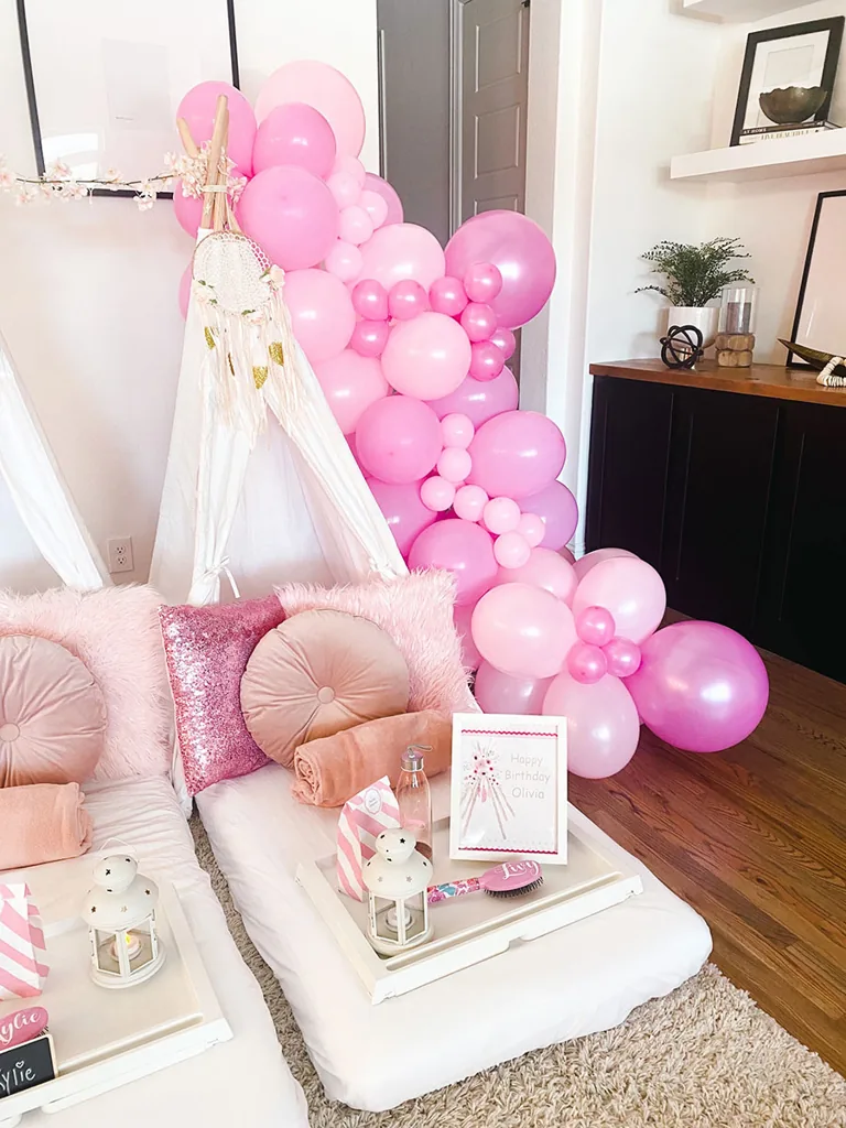 Pink balloon garland framing a white teepee with blush cushions